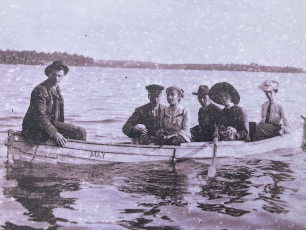 Black and white photo of men and women in small boat on lake.
