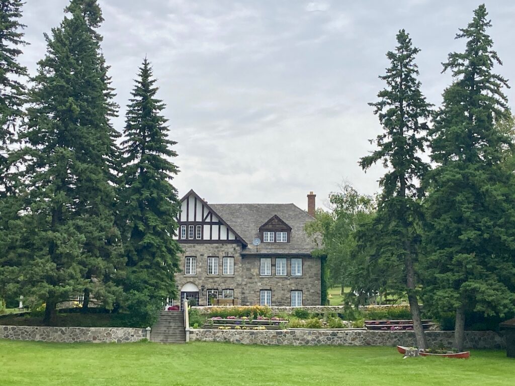 Image of large stone building among evergreen trees.