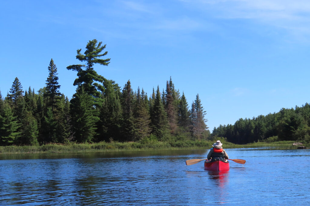 Red canoe with two paddlers on a lake under blue sky.