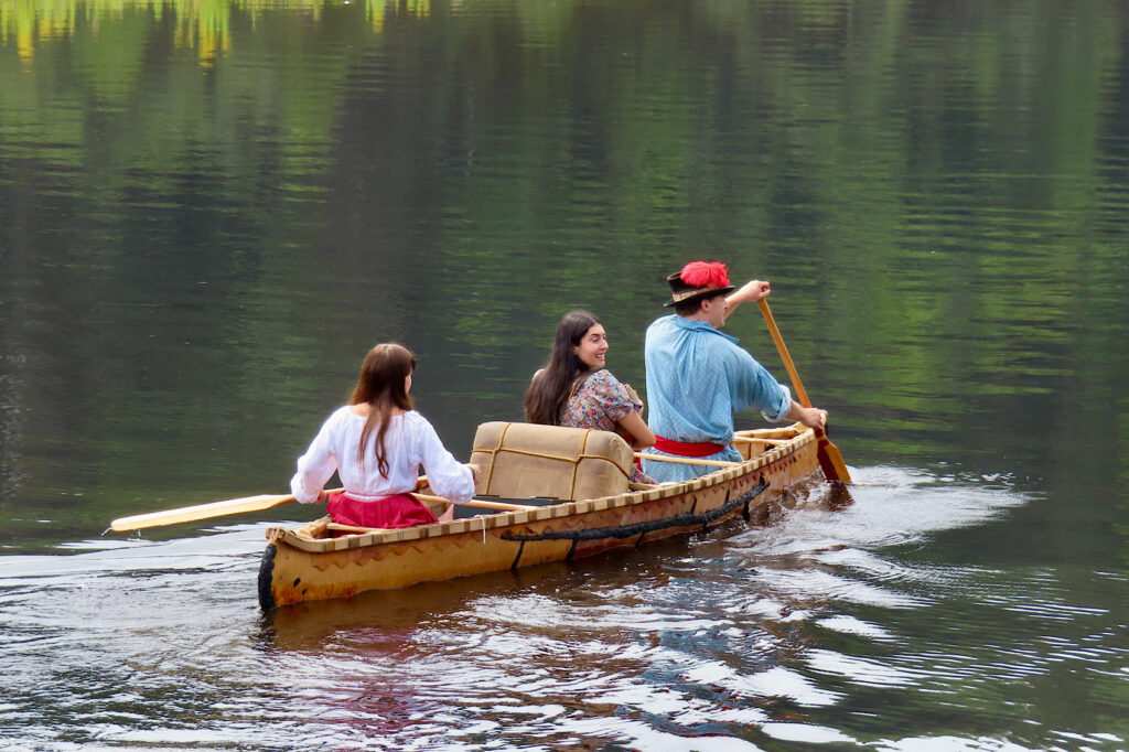 Three people paddling down a river in a birchbark canoe.