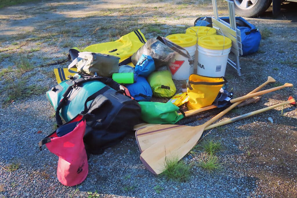 Pile of dry bags, paddles, bucket and miscellaneous canoe gear.