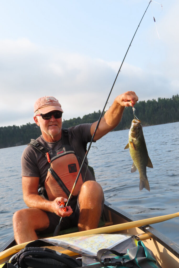 Man holding up fish on lake while in canoe.