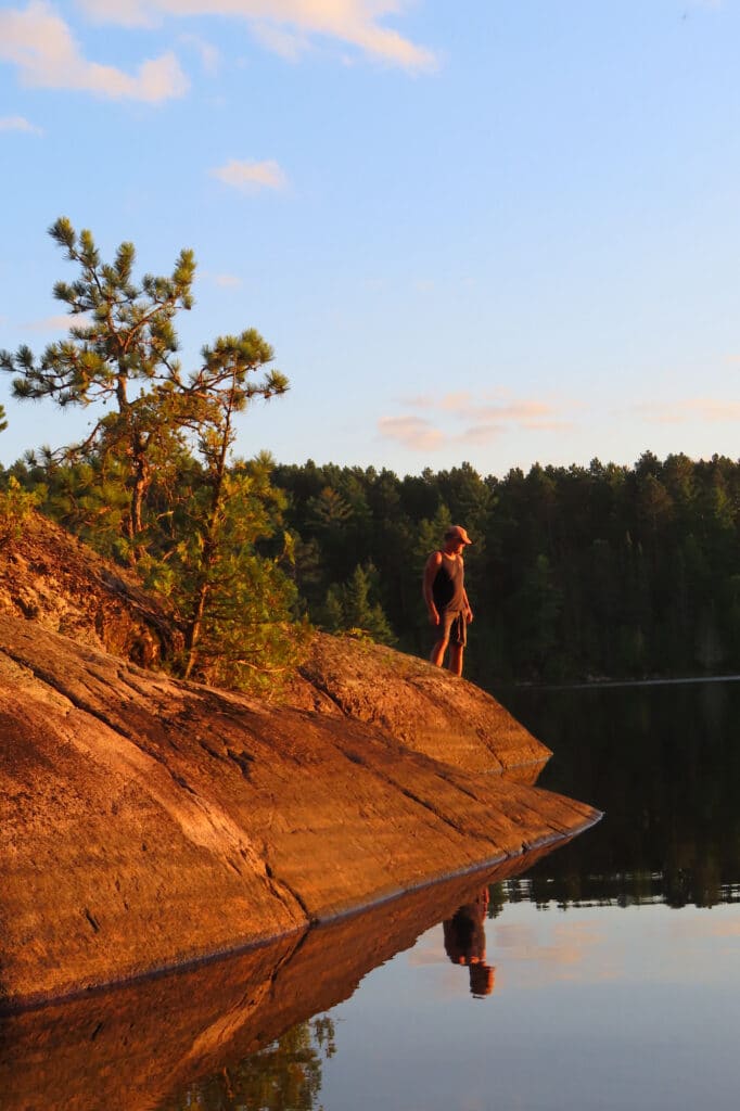 Man standing on rock glowing in sunset light above water.