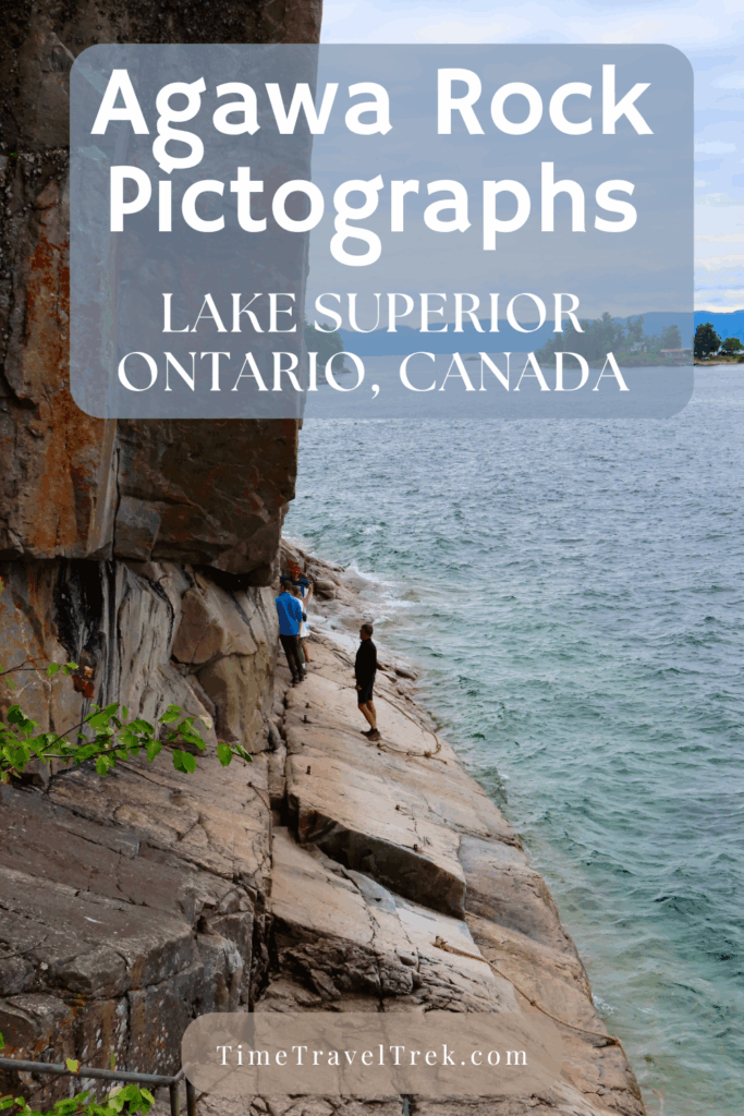 People walking along a narrow rock ledge beside blue lake with cliffs rising above and waves below.
