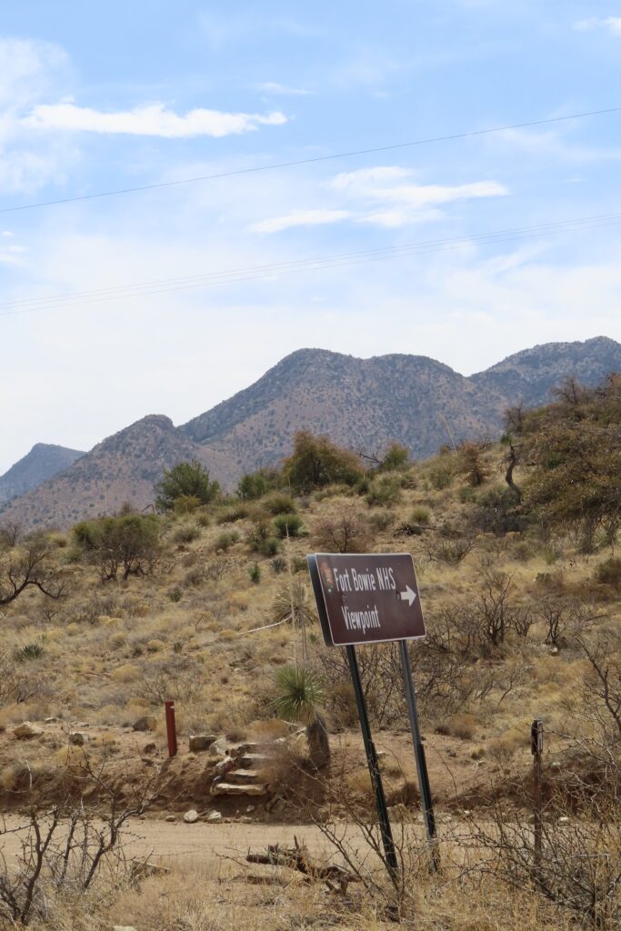 Road sign pointing to Fort Bowie Overlook and a set of rock stairs to a trail.