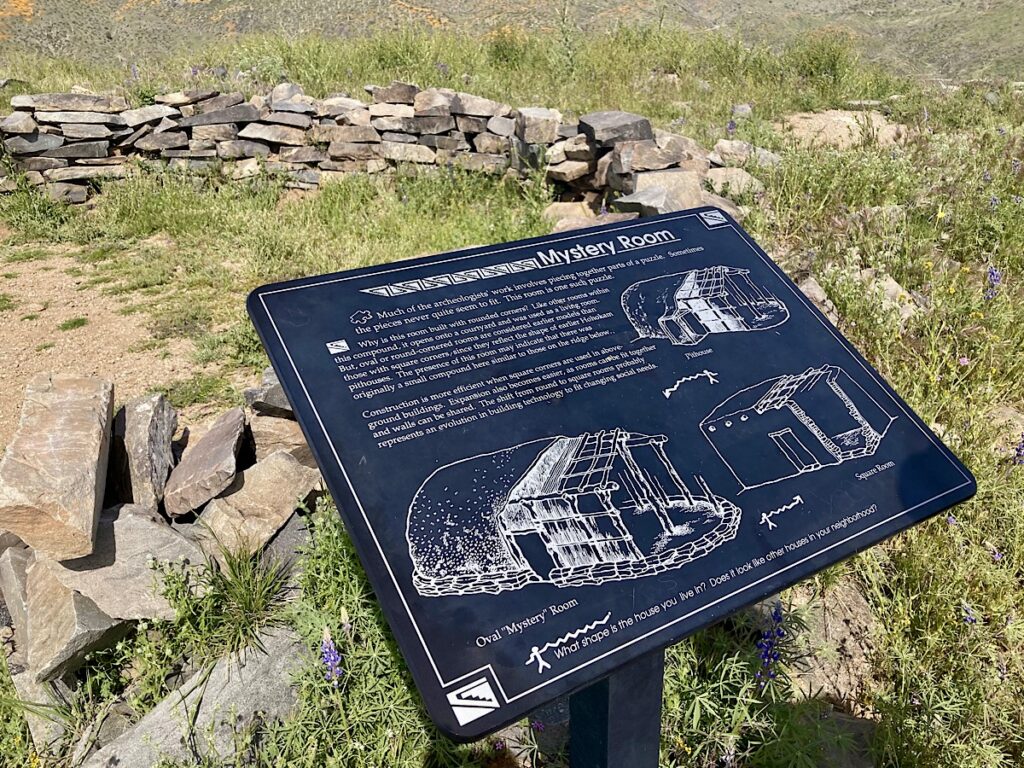 Interpretive sign beside low rock wall.