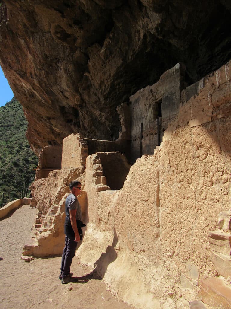 Man standing looking at rock wall of building in a cave.