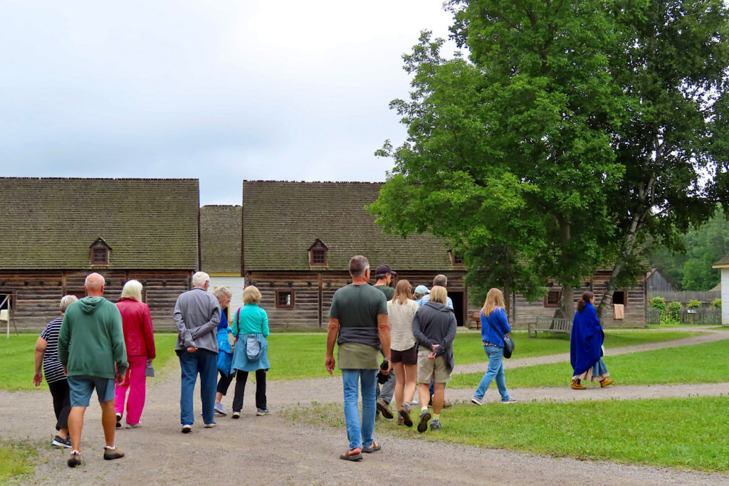 Group of people walking on gravel path past wooden buildings.