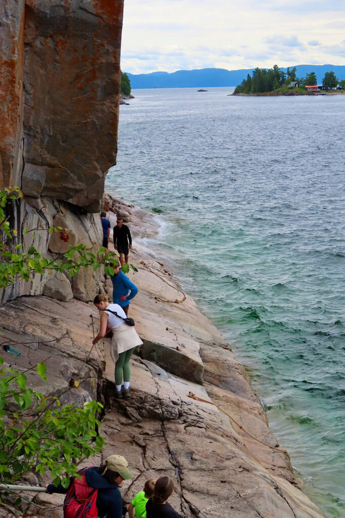 Group of people strung out across angled rock slope above water.