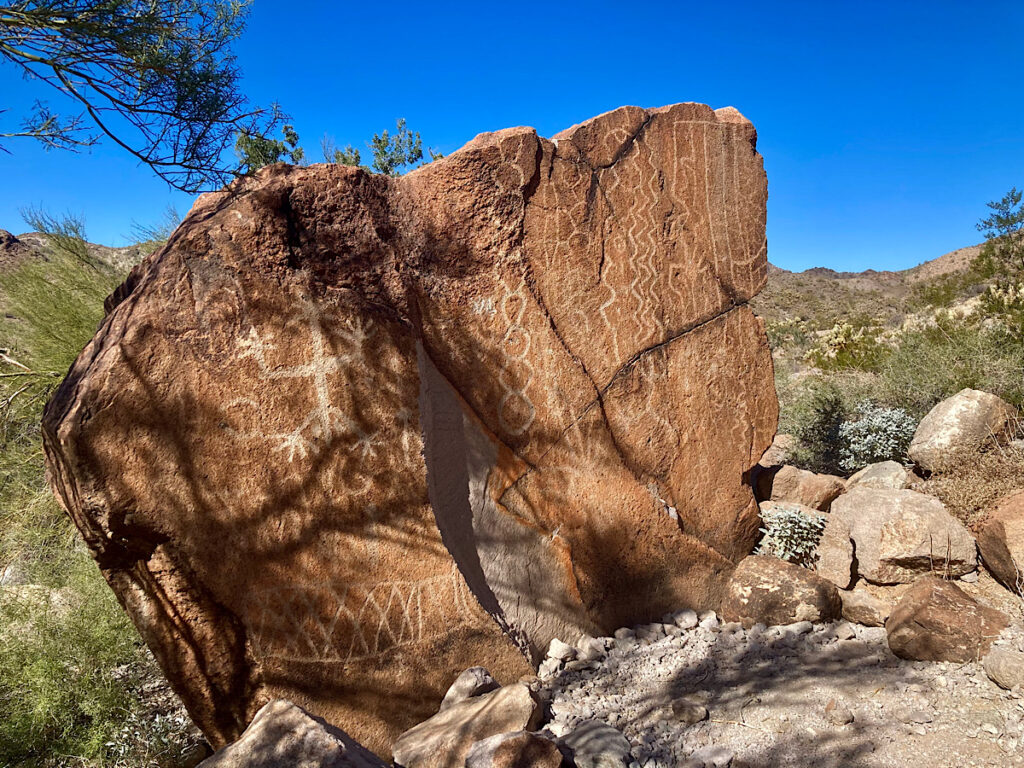 Large blocky rock carved with inscriptions under blue sky.