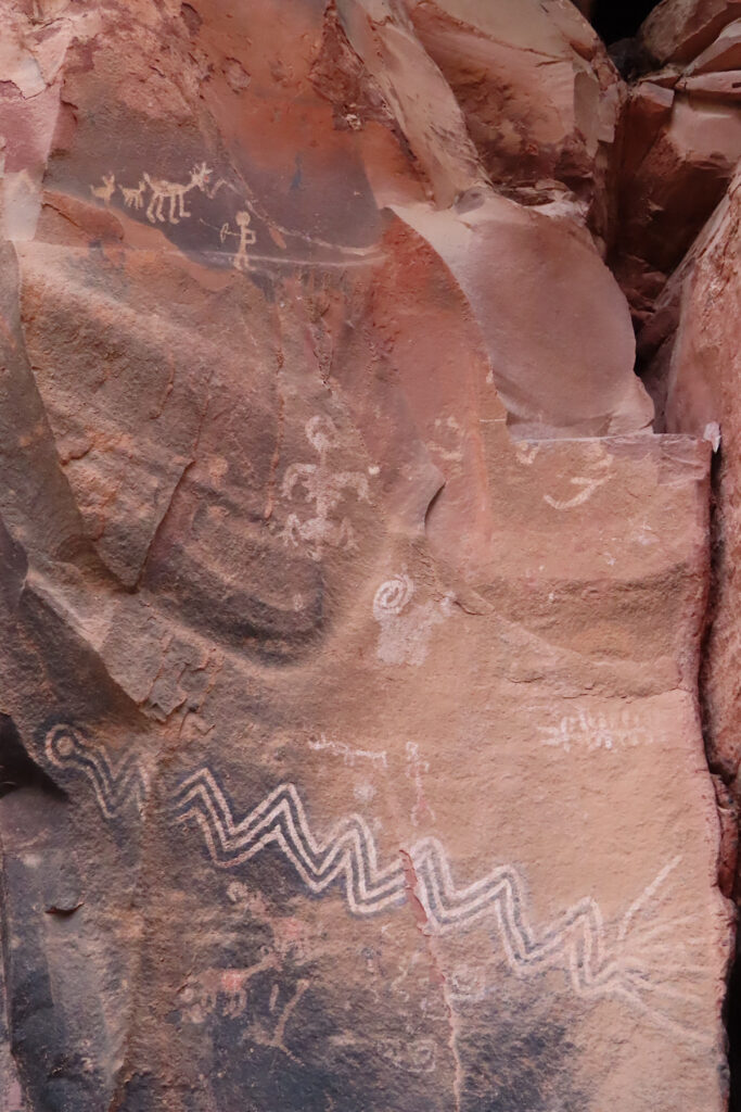 Lines and anthropomorphic figures painted on reddish sandstone rock.