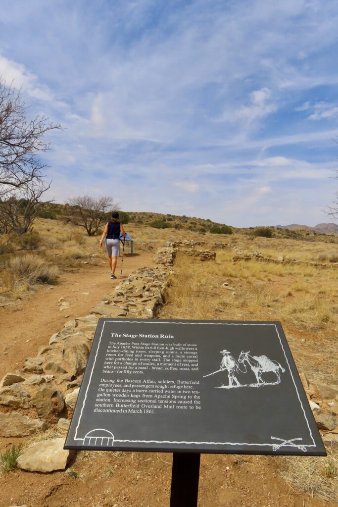 Interpretive sign for Stage Station with woman walking beside rock building outline.