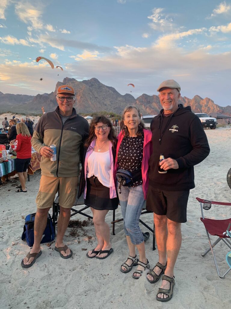 Two men and two women standing on a beah with mountains in background.