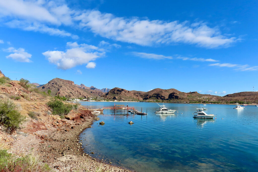 Rugged coastline with boats in shallow blue water bay.