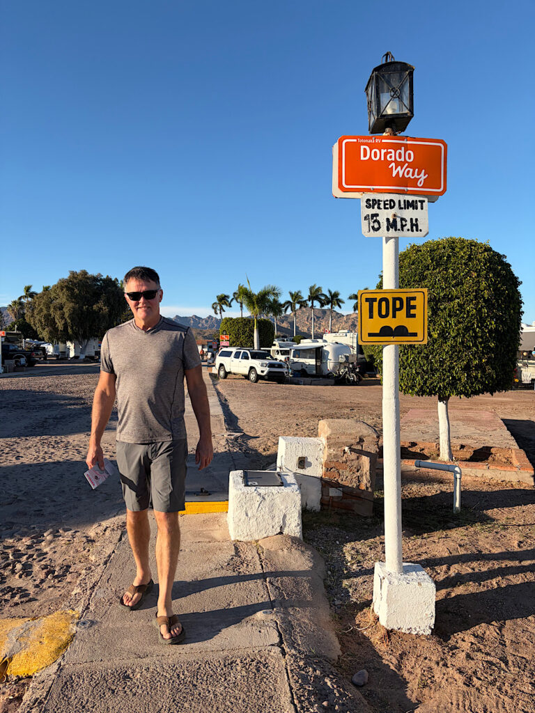 Man walking on sidewalk in trailer park with signs reading Dorado Way and Tope.