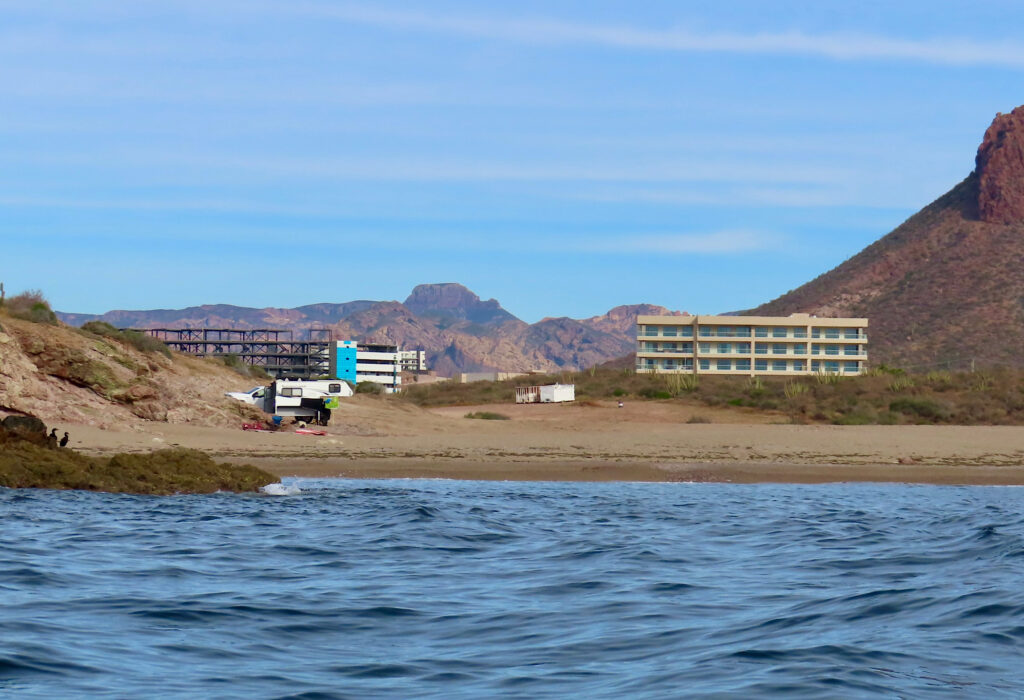 Ocean, beach, camper, building in distance.