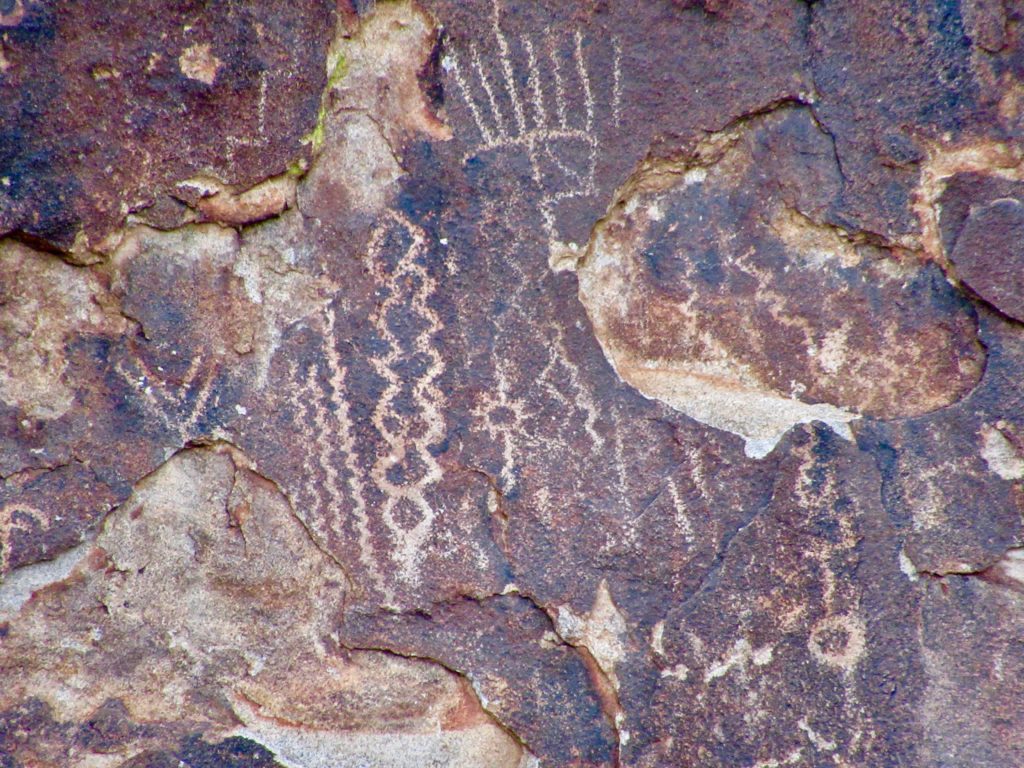 A variety of carved lines and squiggles make lighter images appear on dark rock.