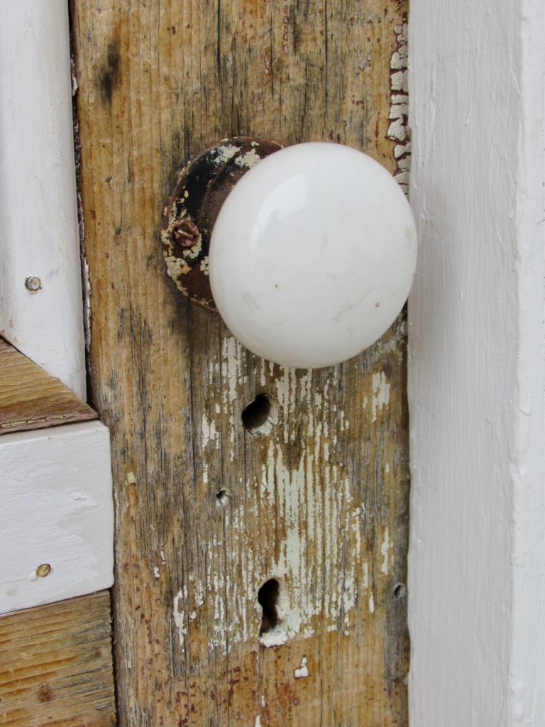 Old, white ceramic door knob on peeling wooden door