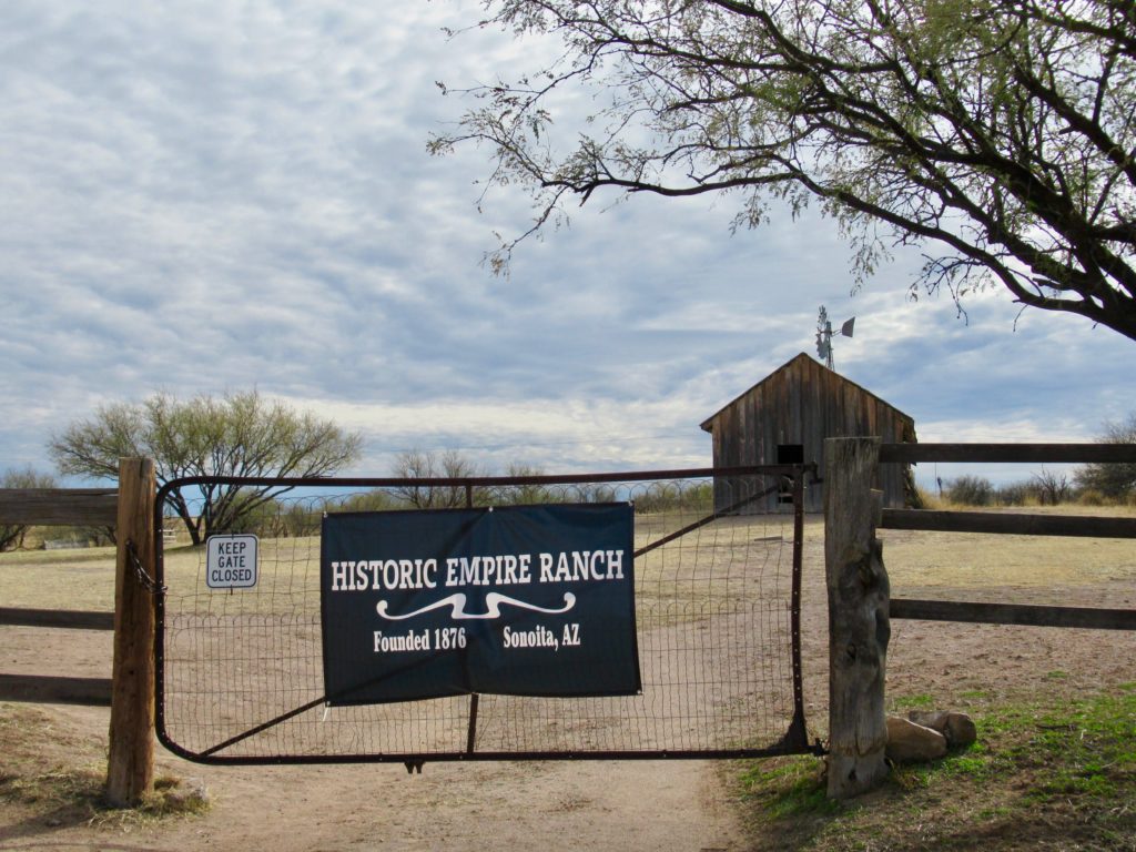 Windmill, barn and a fence with a metal gate. The gate has "Historic Empire Ranch founded in 1876 Sonoita, Arizona" written on it.