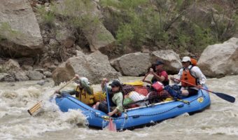 Blue raft with four people and gear paddling through a whitewater rapid