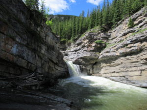 Waterfalls and grey cliffs topped with evergreen trees