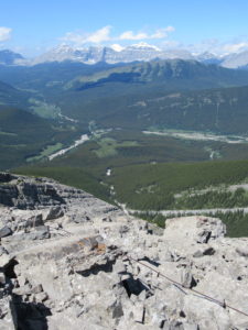 Rocky slope in foreground with treed valley below and mountains in distance