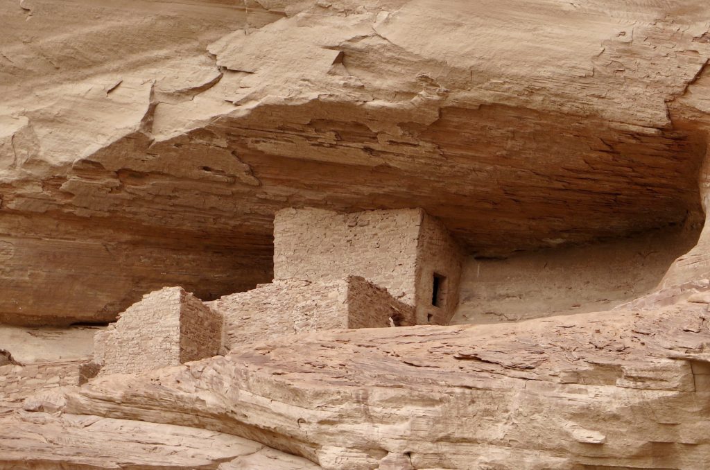 Ancient rock structures in sandstone cliff alcove.