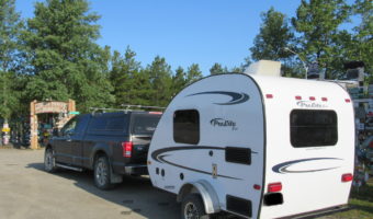 Grey truck and small white trailer parked outside signed entrance reading: Sign Post Forest.