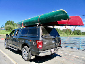 Green and red canoes strapped to roof of Ford F150 pickup truck parked on ferry deck.