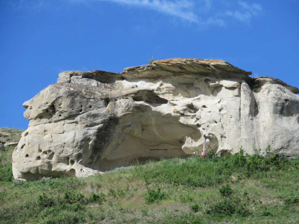Large sandstone cave on top of green hill.