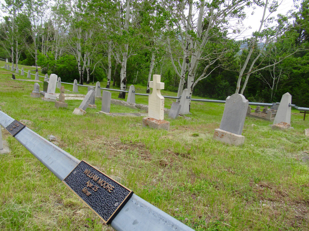 Graveyard with headstones in rows enclosed by metal fence. Plaque on metal fence reads: William Moore, age 25, miner.