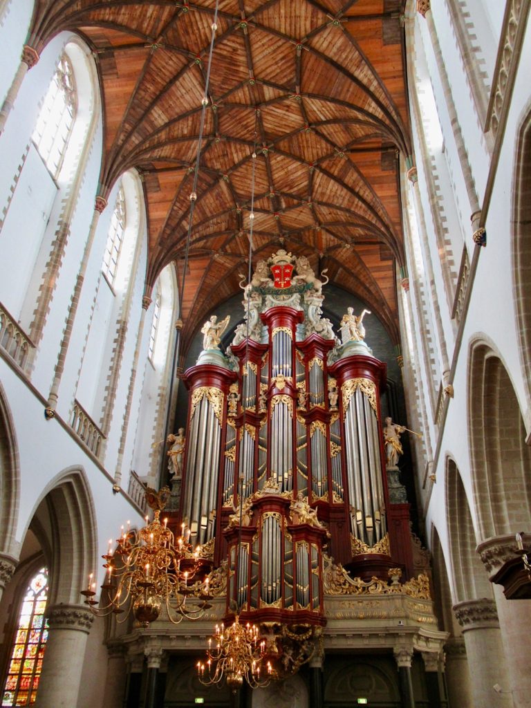 Large pipe organ in church with high wooden ceilings and white-framed arched windows.