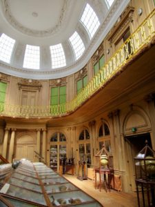 Interior of oval room with intricate woodwork and high white windows.