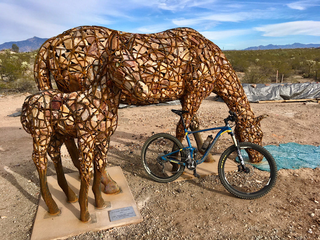 Rock-filled ironwork sculptures of a mare and foal with a mountain bike leaning up against the mare beside bike path in Tucson.