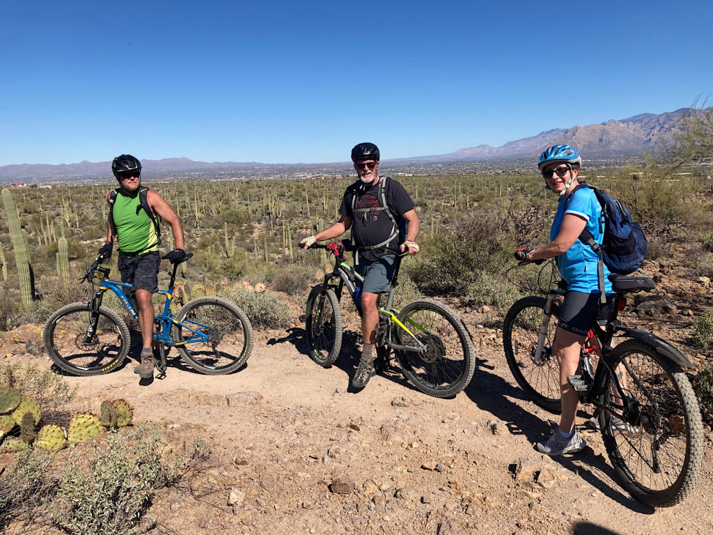 Two men and one woman on mountain bikes looking back at photographer with desert in background.