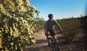 Man on mountain bike riding gravel trail next to large cactus.