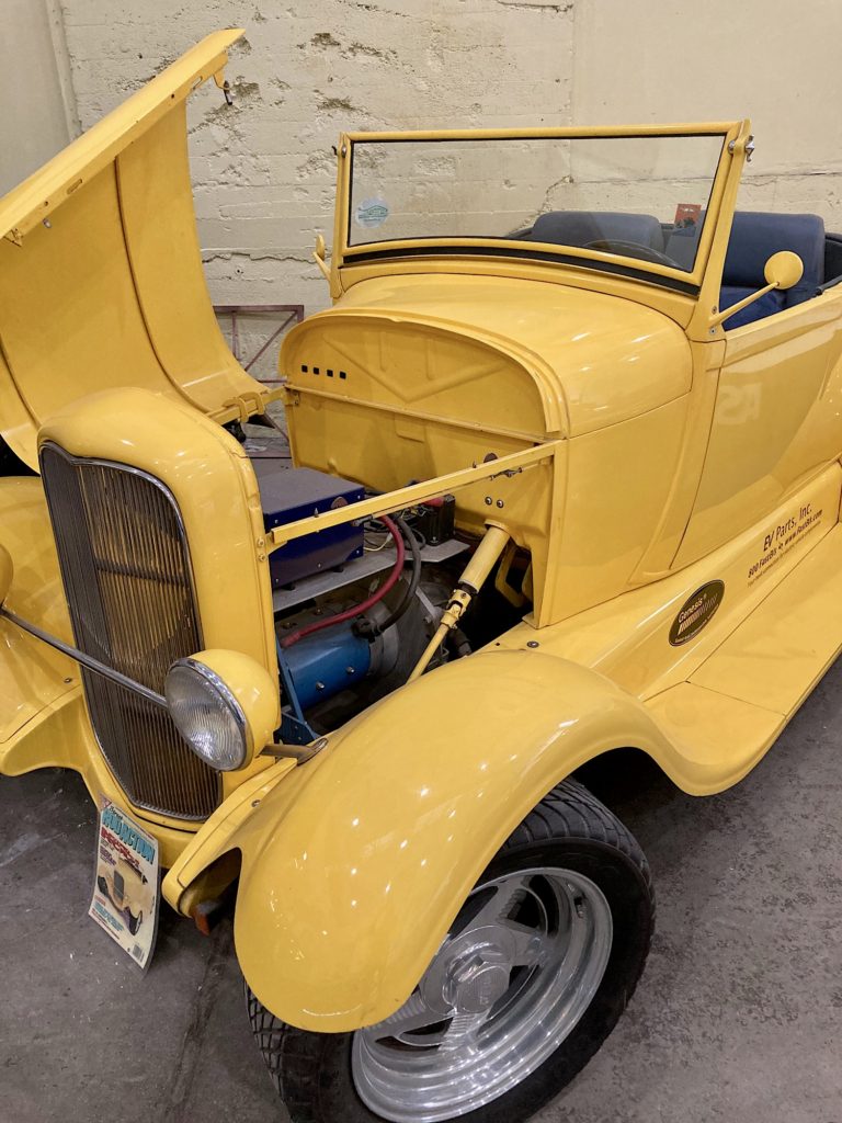 Bright yellow hot rod with front engine compartment open.