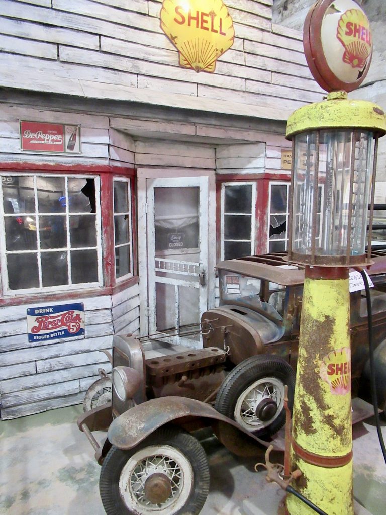 Old fashioned yellow gas pump and vintage car in front of red and white gas station.