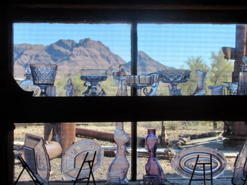 Historic pieces of glassware perched on window frame with mountains in distance.