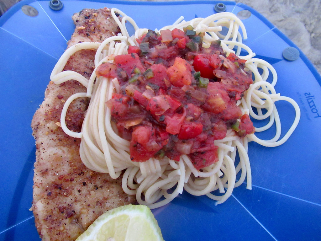 Fried fish fillet with spaghetti and tomato sauce on blue plate.