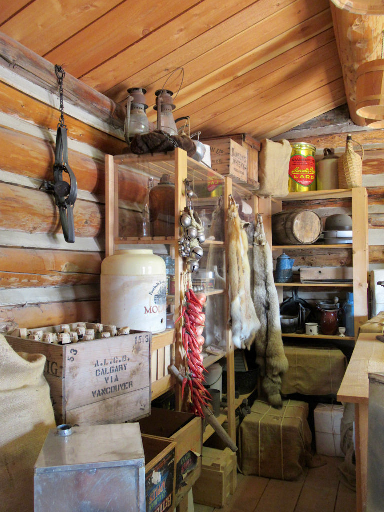 Interior of log building with historic artifacts, furs and trade goods on shelves.