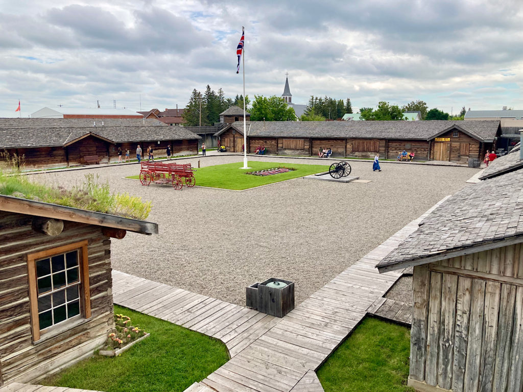 Gravel courtyard ringed with wooden building and a centre flagpole in grassy area.