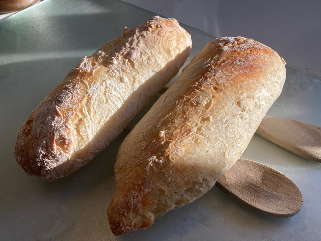 Two crusty baguettes sitting on wooden spoons on a counter.