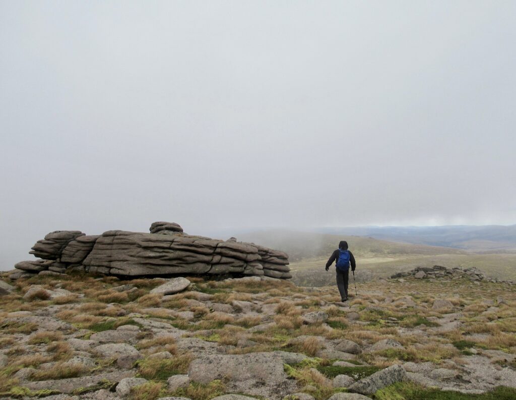 Distance image of man hiking beside rugged rock formation under misty skies.
