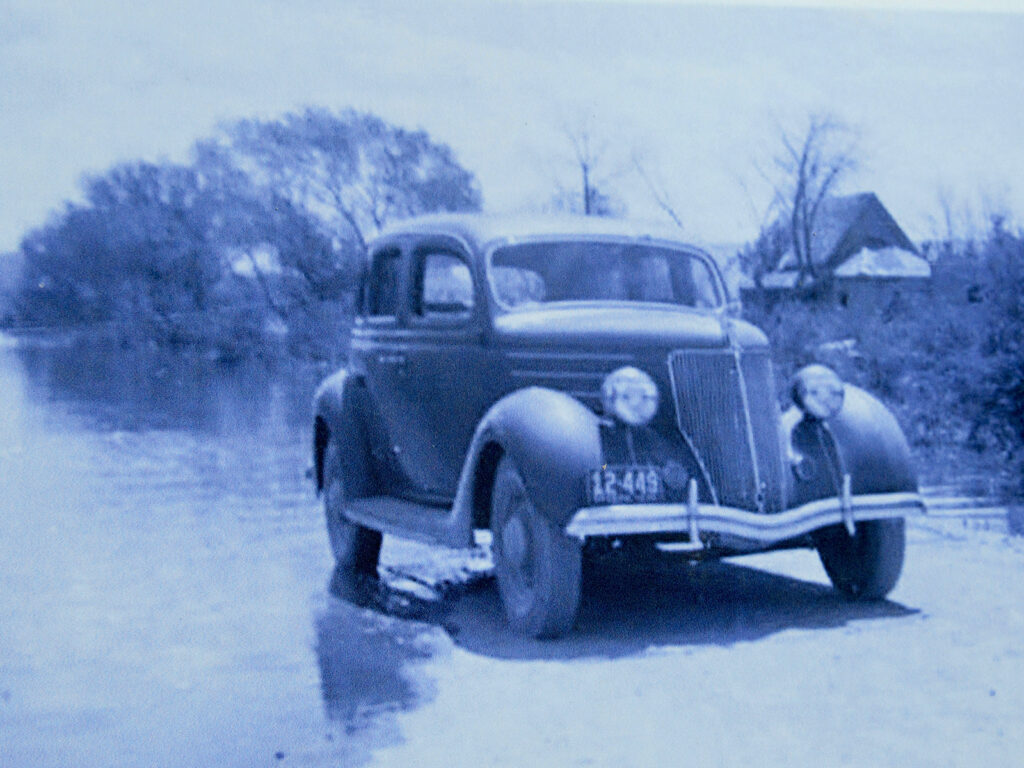 Black and white photo of 1930s era car on edge to water.