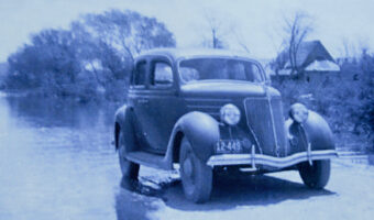 Black and white photo of 1930s era car on edge to water.