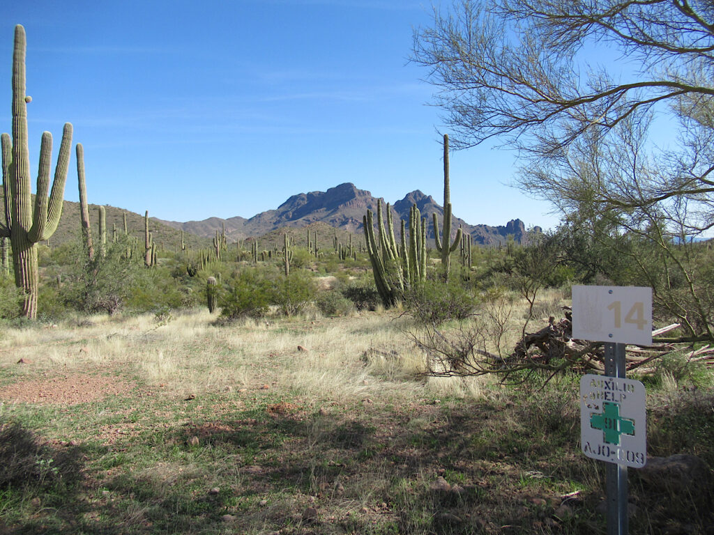 White sign with number 14 in front of desert landscape and distant mountains under blue sky.