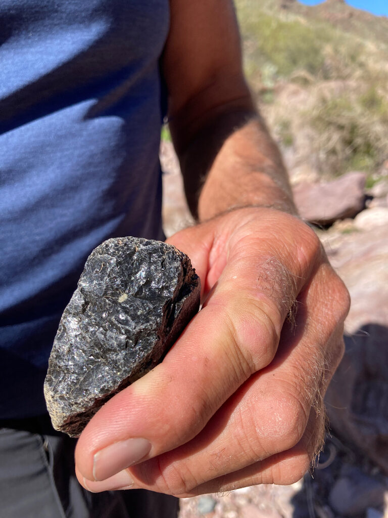 Man in blue shirt hold shiny black rock in his hand.
