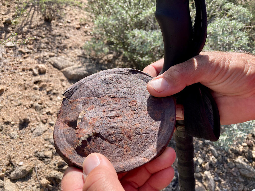 Rusy metal lid of a tin held in hands of a hiker. It reads: A Shilling Product.