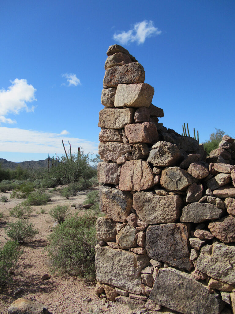 Partial rock wall of building in desert under blue sky.